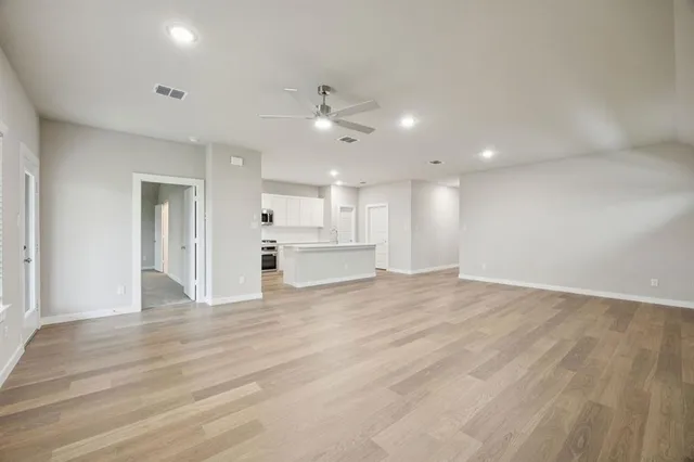 a view of an empty room with wooden floor and a kitchen
