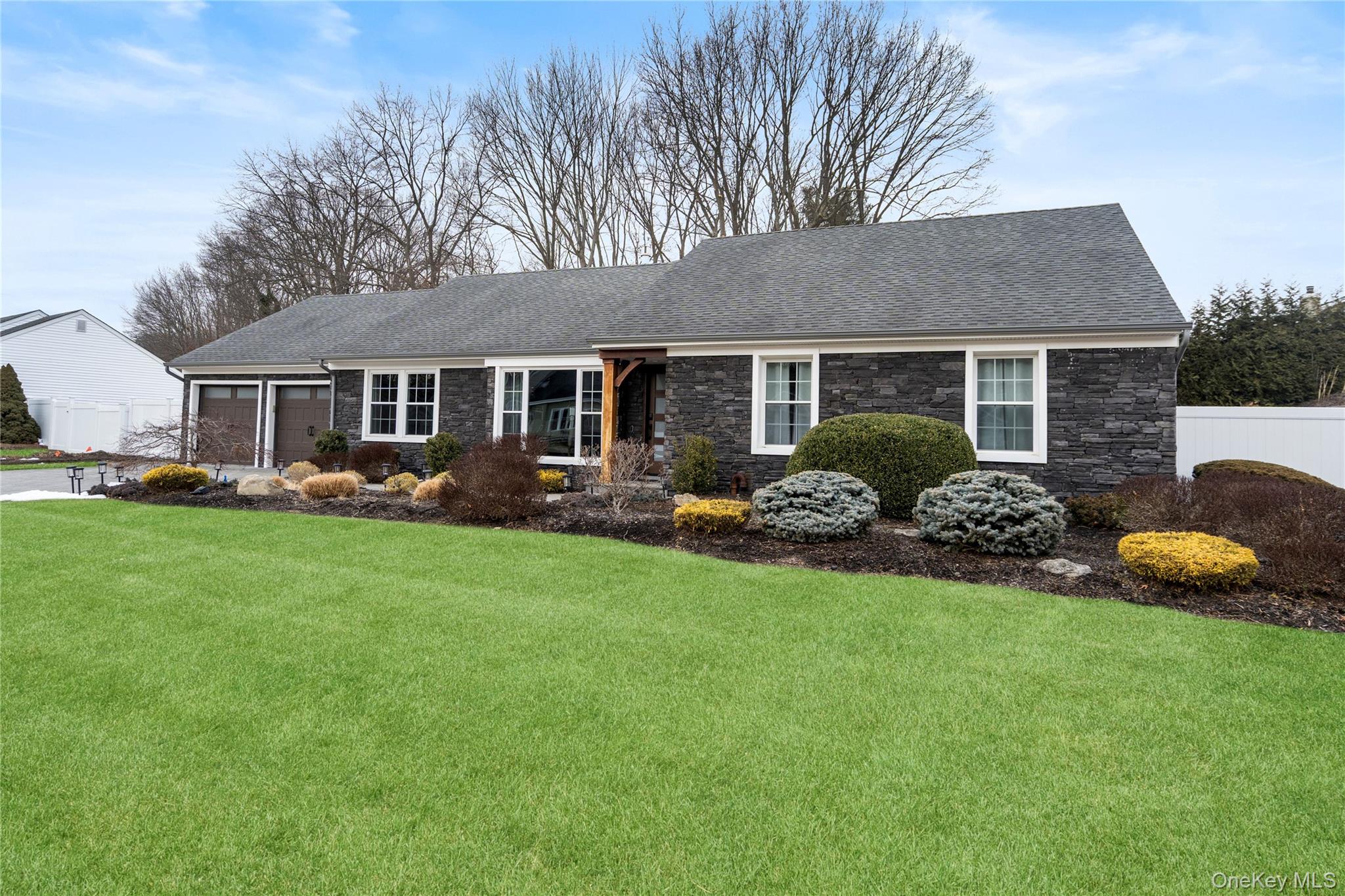 Ranch-style house with stone siding, a garage, and roof with shingles