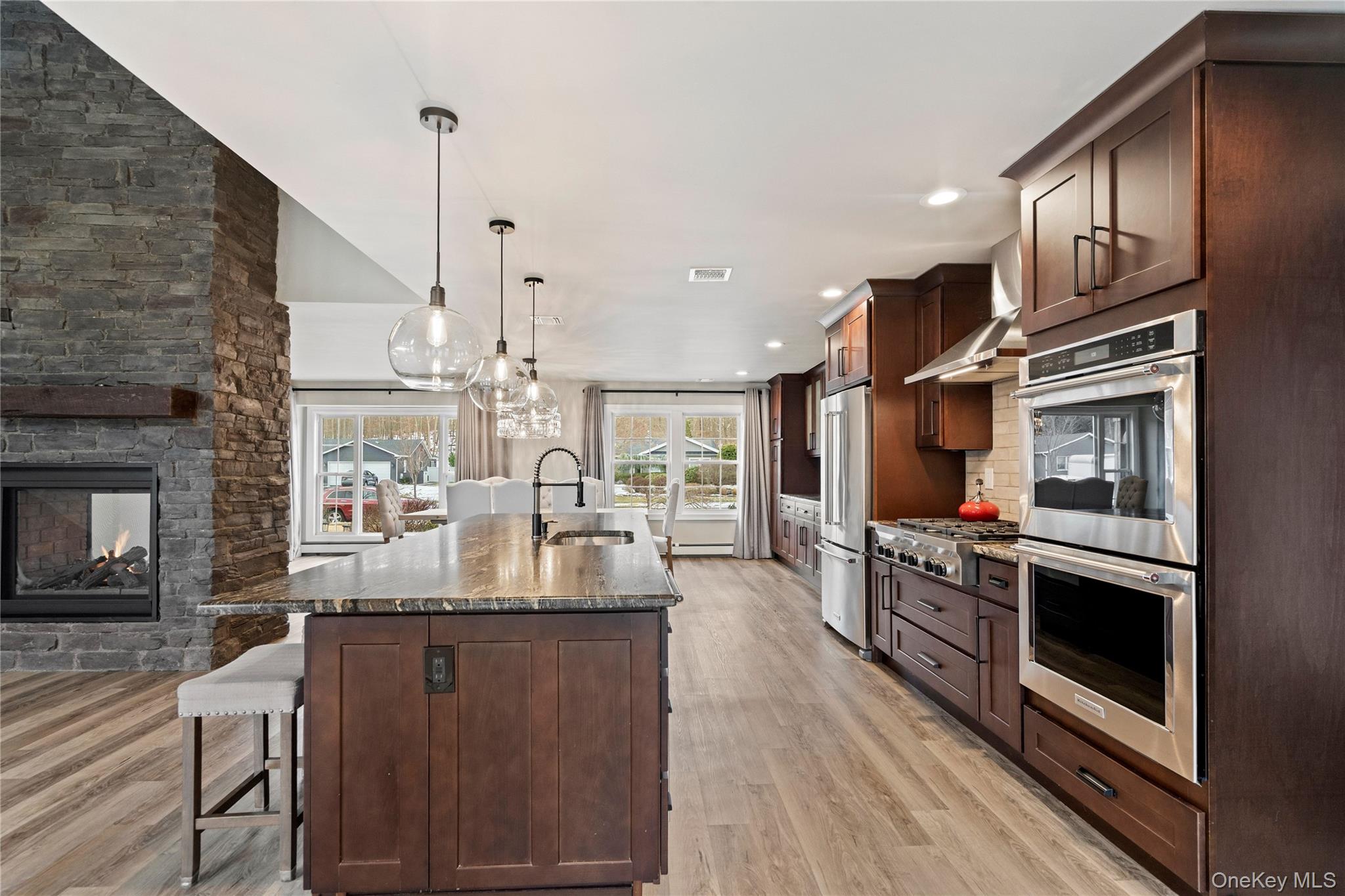 58 Timber Ridge Drive Commack, NY 11725 - Photo 14 of 34 Kitchen featuring dark stone countertops, a kitchen bar, dark brown cabinetry, pendant lighting, and appliances with stainless steel finishes