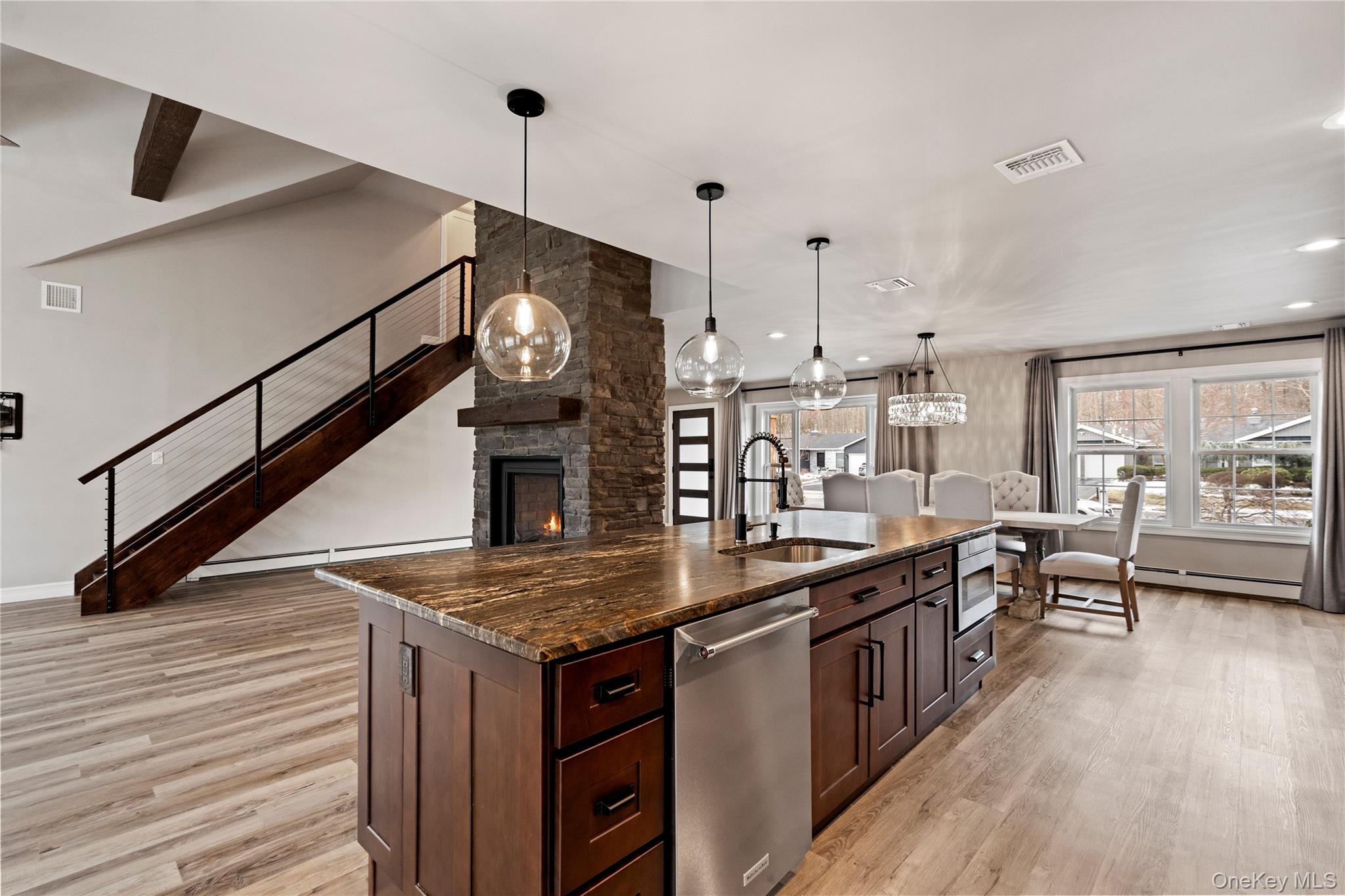 58 Timber Ridge Drive Commack, NY 11725 - Photo 15 of 34 Kitchen featuring a stone fireplace, a center island with sink, dark brown cabinets, decorative light fixtures, and dishwasher