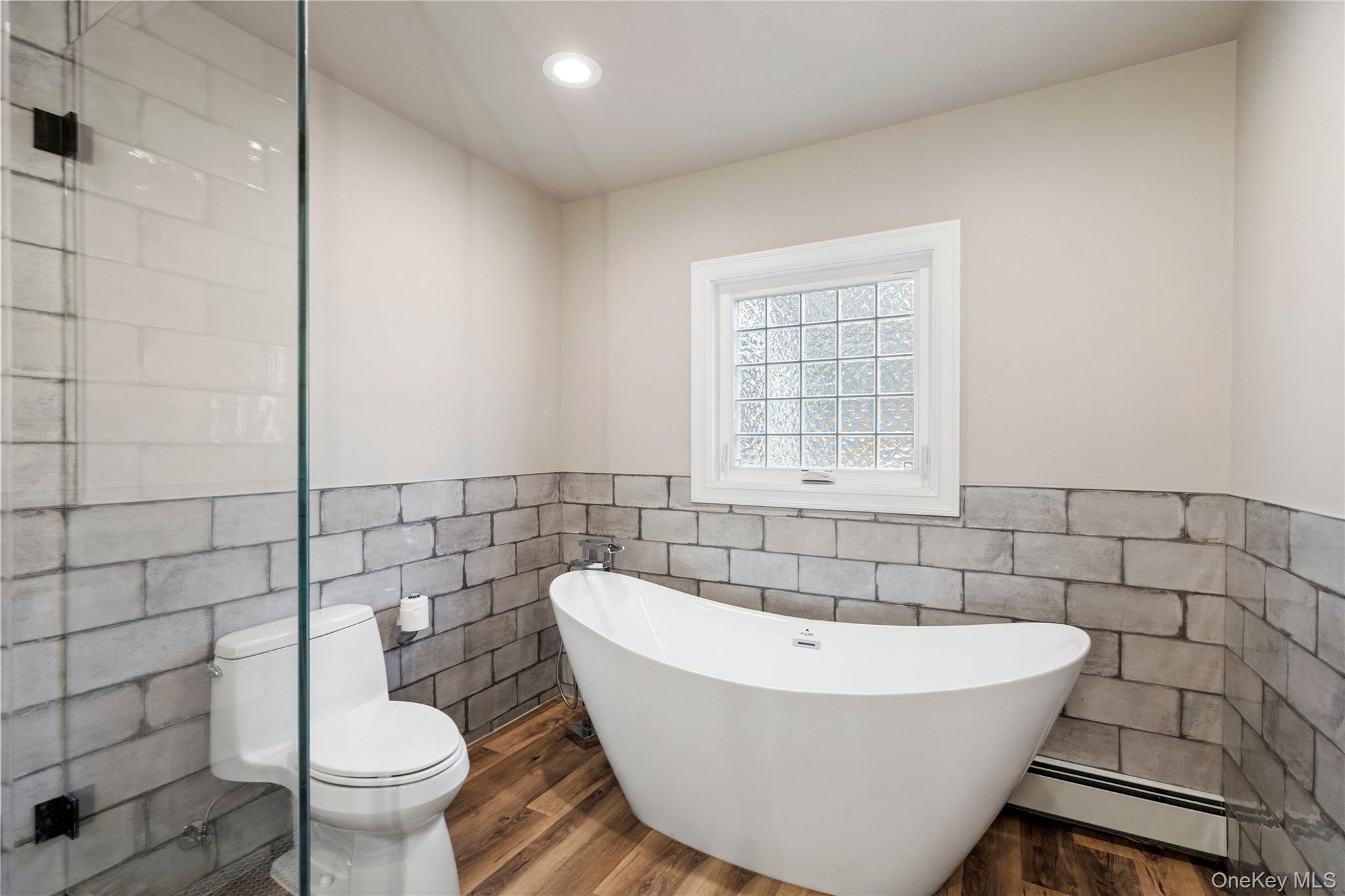 58 Timber Ridge Drive Commack, NY 11725 - Photo 21 of 34 Full bathroom with a wainscoted wall, tile walls, a freestanding tub, a baseboard heating unit, and recessed lighting