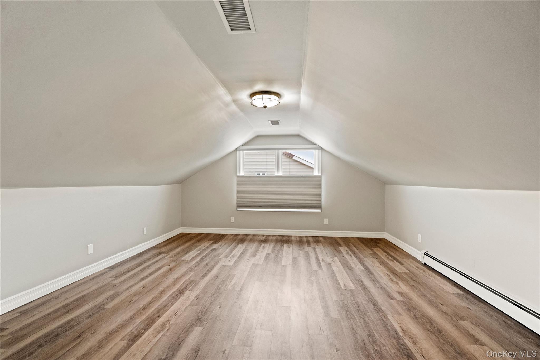 58 Timber Ridge Drive Commack, NY 11725 - Photo 27 of 34 Additional living space with baseboard heating, vaulted ceiling, and light wood-style flooring