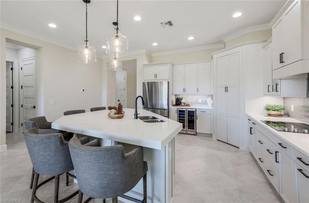 8850 Calypso Court Naples, FL 34113 - Photo 11 of 41 Kitchen featuring a breakfast bar area, crown molding, freestanding refrigerator, hanging light fixtures, and tasteful backsplash