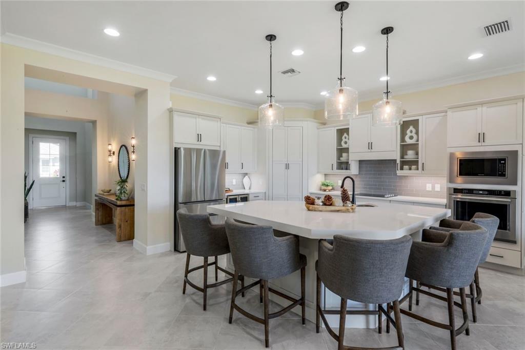 8850 Calypso Court Naples, FL 34113 - Photo 13 of 41 Kitchen with pendant lighting, white cabinetry, stainless steel appliances, glass insert cabinets, and a breakfast bar area