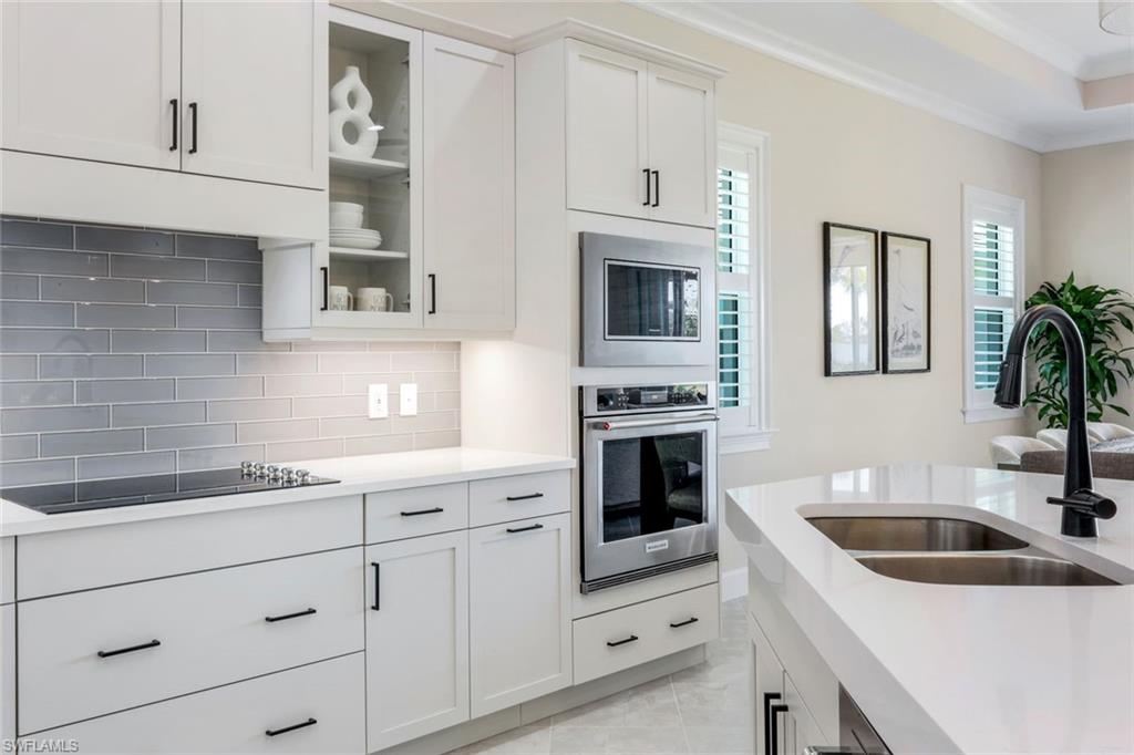 8850 Calypso Court Naples, FL 34113 - Photo 10 of 41 Kitchen with white cabinets, appliances with stainless steel finishes, decorative backsplash, light stone countertops, and crown molding