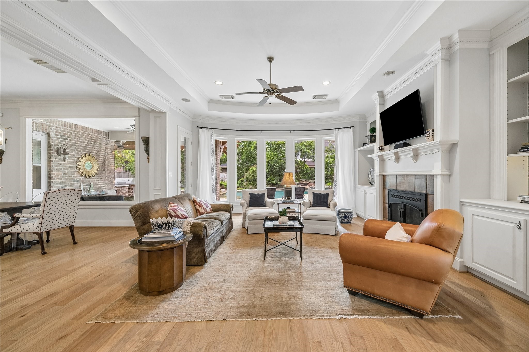 11421 Whippoorwill Road Houston, TX 77024 - Photo 11 of 33 Bright and spacious family room featuring a spectacular curved window wall overlooking the pool and lush backyard. Highlights include a brick-hearth fireplace, integrated custom cabinetry, and a double-tray ceiling with recessed lighting.