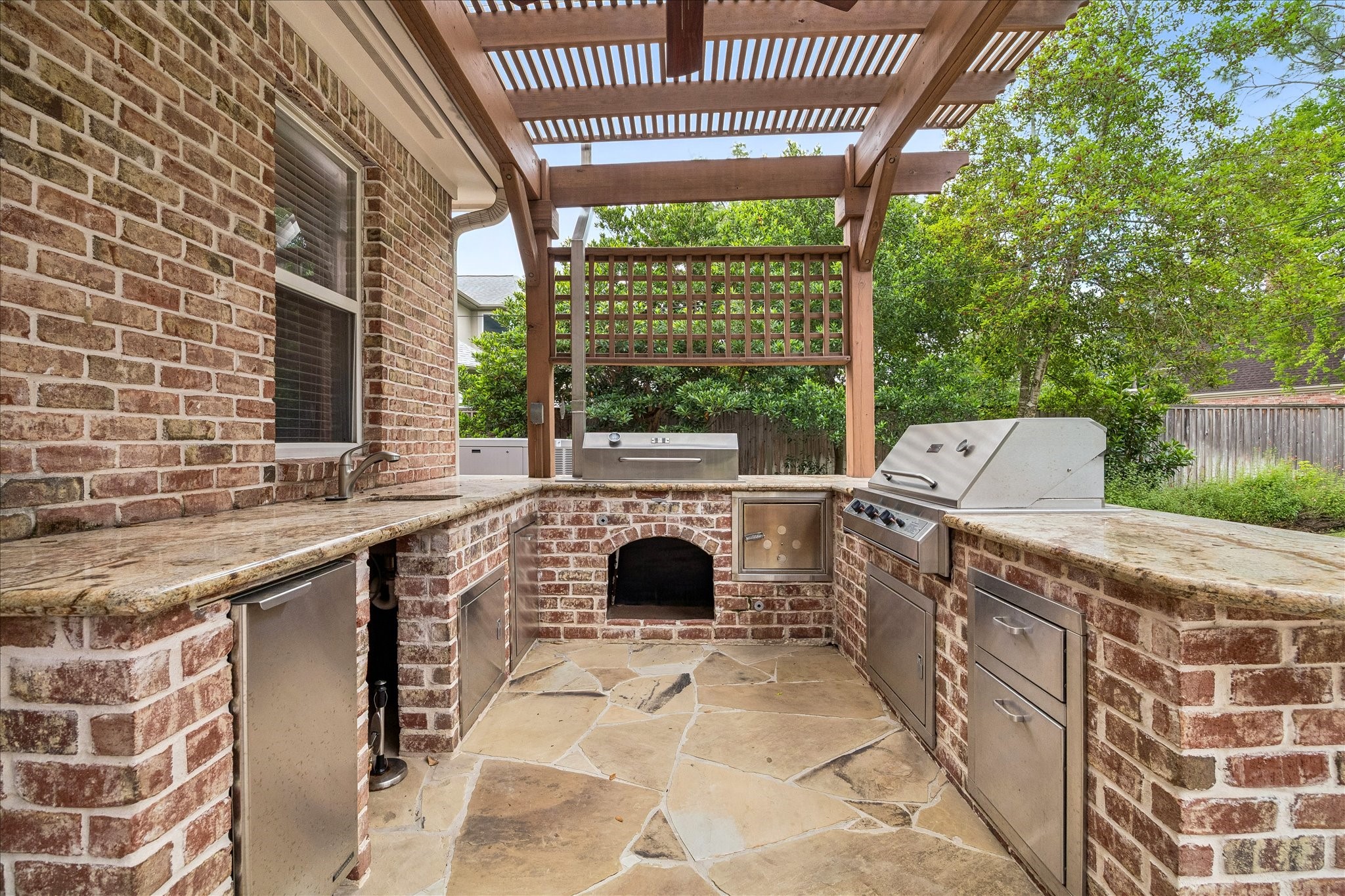 11421 Whippoorwill Road Houston, TX 77024 - Photo 26 of 33 Pro-grade outdoor kitchen with built-in grill, burners, and cooling. Highlights include a wood fired hearth, granite counters, and a decorative wood pergola. Set on a beautiful flagstone patio, it’s the ultimate station for poolside hosting.