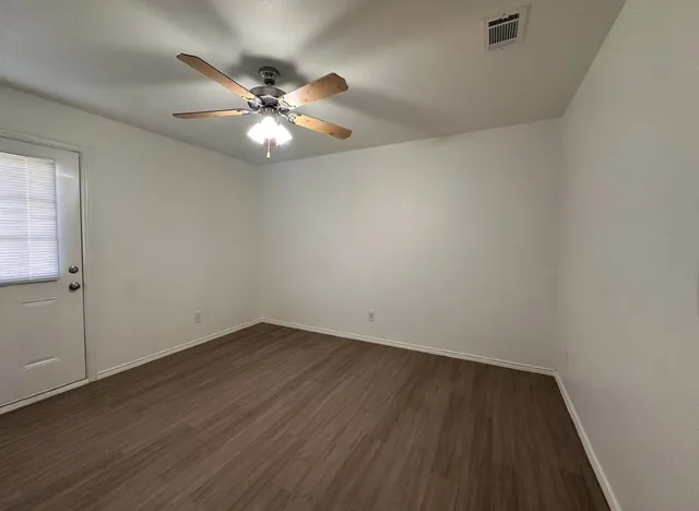 an empty room with wooden floor fan and windows