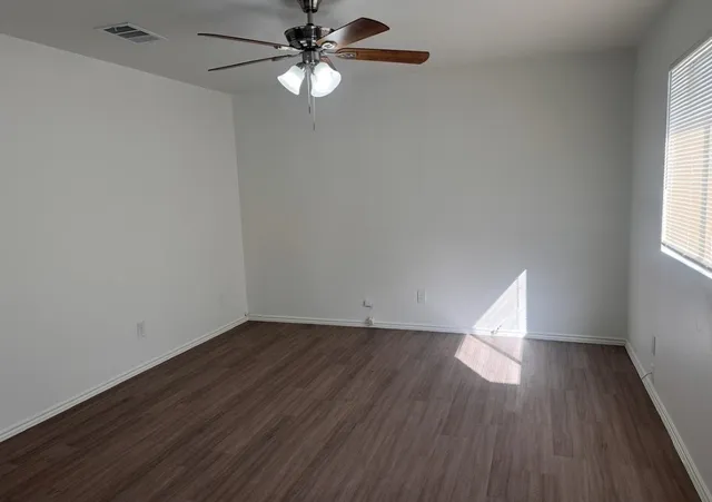 an empty room with wooden floor fan and windows