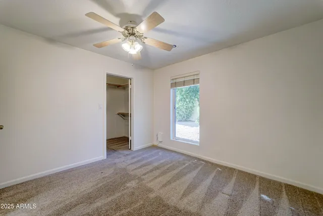 an empty room with chandelier fan and windows