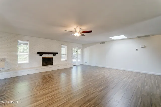 an empty room with wooden floor ceiling fan and windows