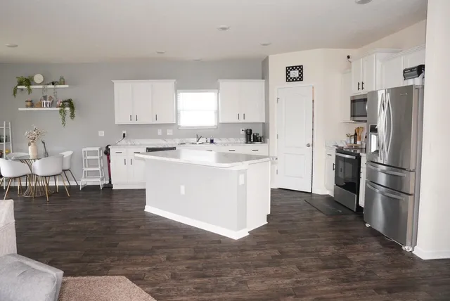 a kitchen with stainless steel appliances kitchen island granite countertop a refrigerator a stove and white cabinets with wooden floor