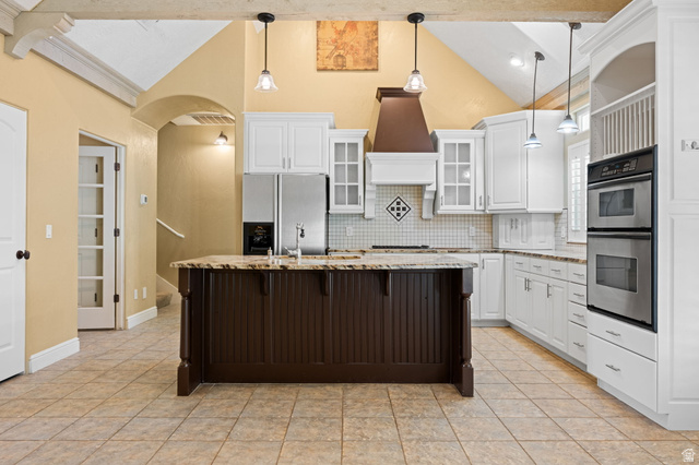 20 Valley Road Leeds, UT 84746 - Photo 3 of 57 Kitchen featuring a large island with built-in cabinetry, white perimeter cabinetry, stainless steel appliances, tile flooring, and vaulted ceilings with exposed beams