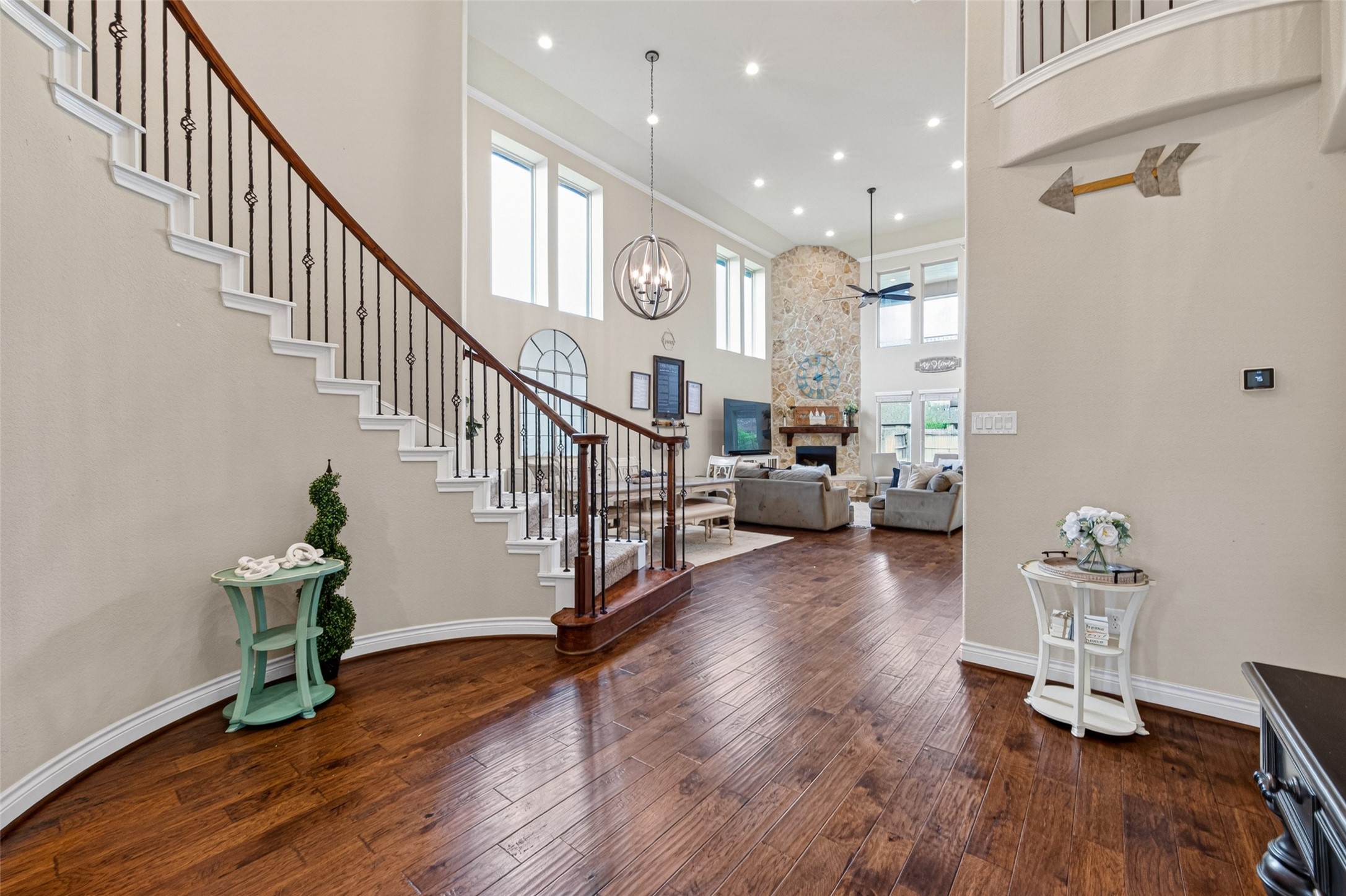 25611 Ellis Ridge Court Katy, TX 77494 - Photo 47 of 49 This photo showcases a spacious and elegant living area with high ceilings, large windows, and a beautiful stone fireplace. The open floor plan connects to a stylish curved staircase, creating a welcoming and airy atmosphere. Perfect for modern family living.