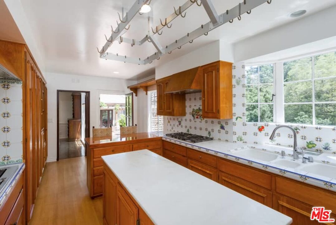 1957 Mandeville Canyon Road Los Angeles, CA 90049 - Photo 23 of 54 a dining room with stainless steel appliances granite countertop a sink dishwasher and a flat tv screen next to a large window with wooden floor