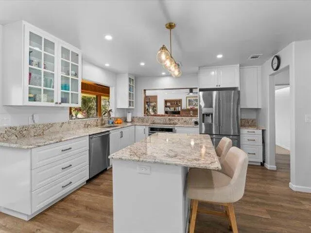 a kitchen with stainless steel appliances granite countertop a refrigerator a sink dishwasher a dining table and chairs with wooden floor