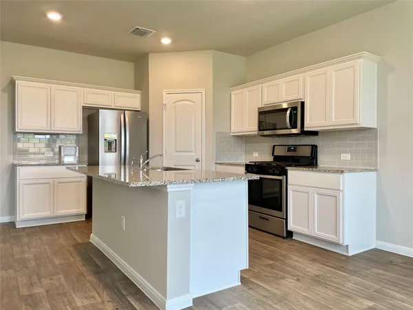 a kitchen with stainless steel appliances a stove top oven a sink a refrigerator and white cabinets