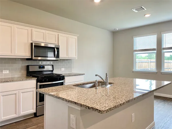 a kitchen with granite countertop a sink a stove and cabinets