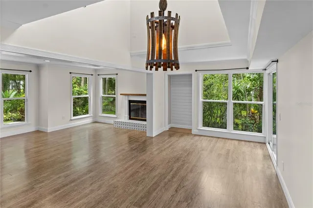 an empty room with wooden floor chandelier and windows