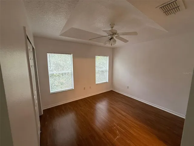 an empty room with wooden floor fan and windows