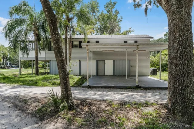 a view of a white house next to a yard with large trees
