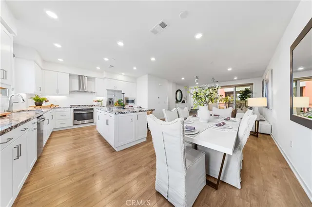 a large white dining hall with stainless steel appliances granite countertop a stove oven a dining table and chairs with wooden floor