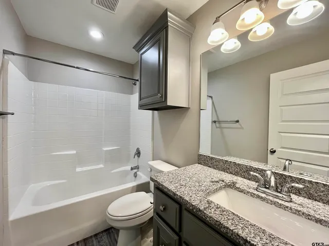 a bathroom with a granite countertop sink a toilet a mirror a bathtub and shower