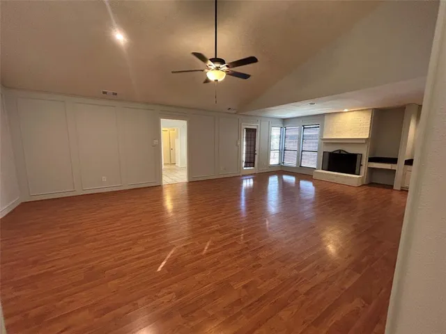 an empty room with wooden floor fireplace and windows
