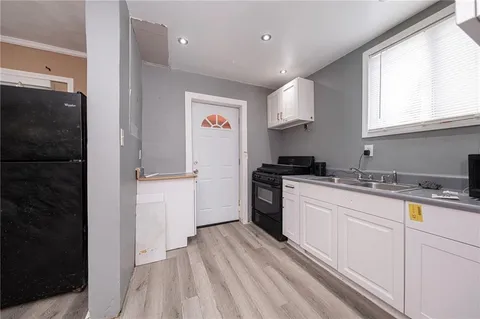 a kitchen with a sink dishwasher a refrigerator and white cabinets with wooden floor