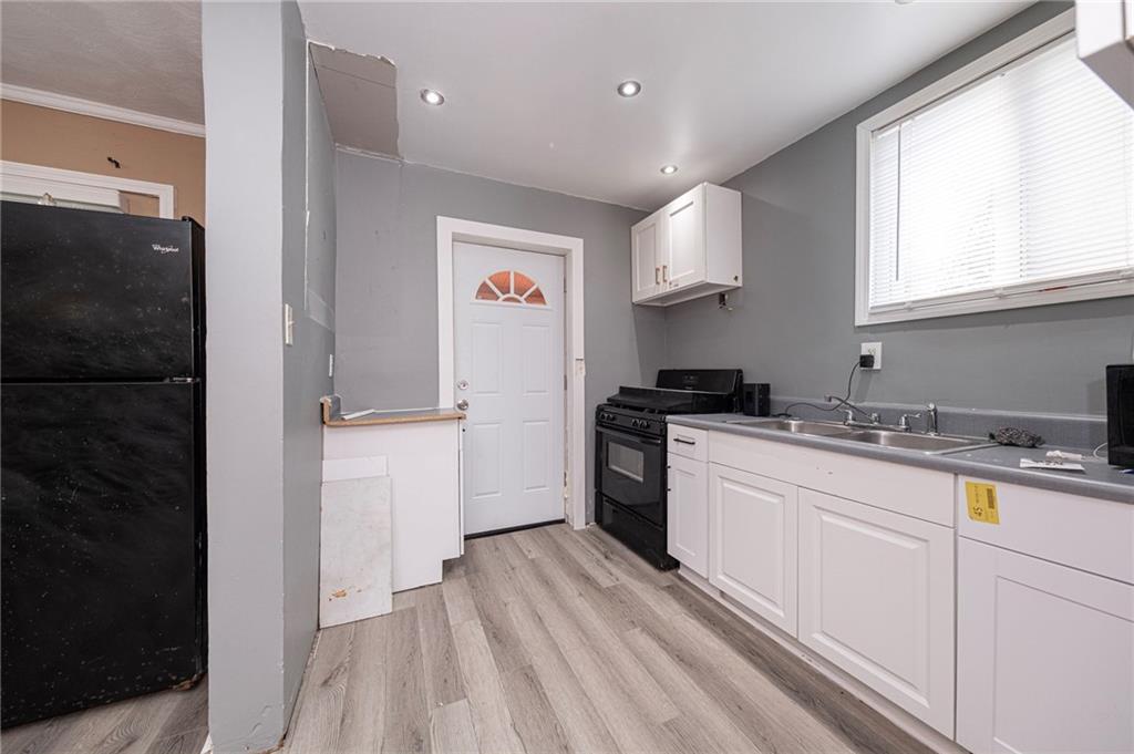 1536 Hunter Street Pittsburgh, PA 15221 - Photo 6 of 18 a kitchen with a sink dishwasher a refrigerator and white cabinets with wooden floor