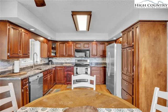 a kitchen with stainless steel appliances granite countertop a refrigerator a sink dishwasher a dining table and chairs with wooden floor