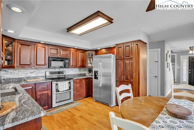 a kitchen with stainless steel appliances granite countertop a stove top oven a sink dishwasher a dining table and chairs with wooden floor