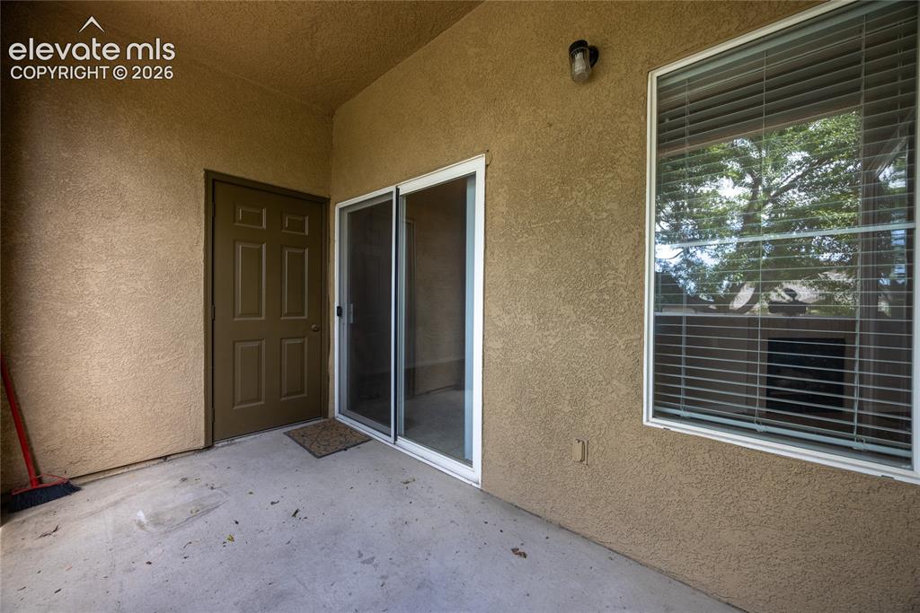 3864 Riviera Grove, Unit 102 Colorado Springs, CO 80922 - Photo 21 of 24 Private patio featuring textured stucco exterior, a sliding glass door, a multi-pane window with blinds, and an exterior light fixture