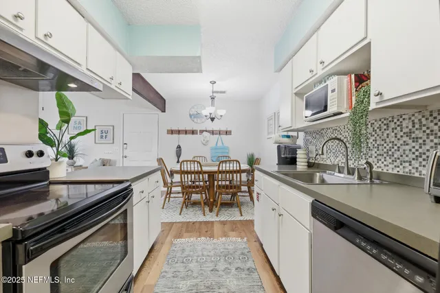 a kitchen with stainless steel appliances granite countertop a sink a refrigerator a stove and white cabinets with wooden floor