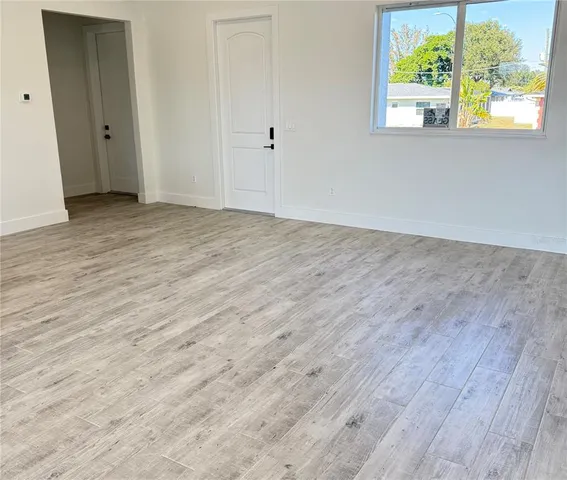 a view of an empty room with wooden floor and a window