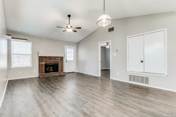a view of an empty room with wooden floor fireplace and a window