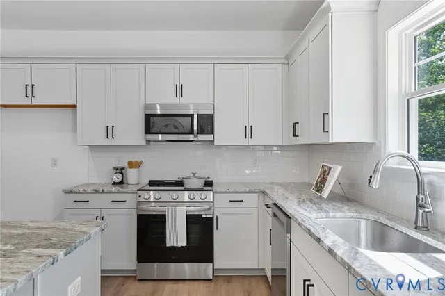 a kitchen with stainless steel appliances granite countertop a sink stove and white cabinets with wooden floor