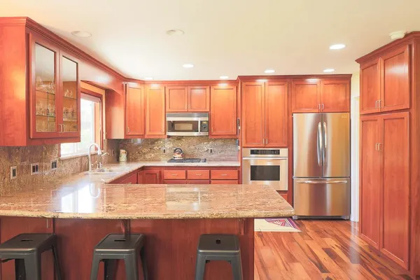 a kitchen with stainless steel appliances granite countertop a refrigerator a sink dishwasher and wooden cabinets with wooden floor