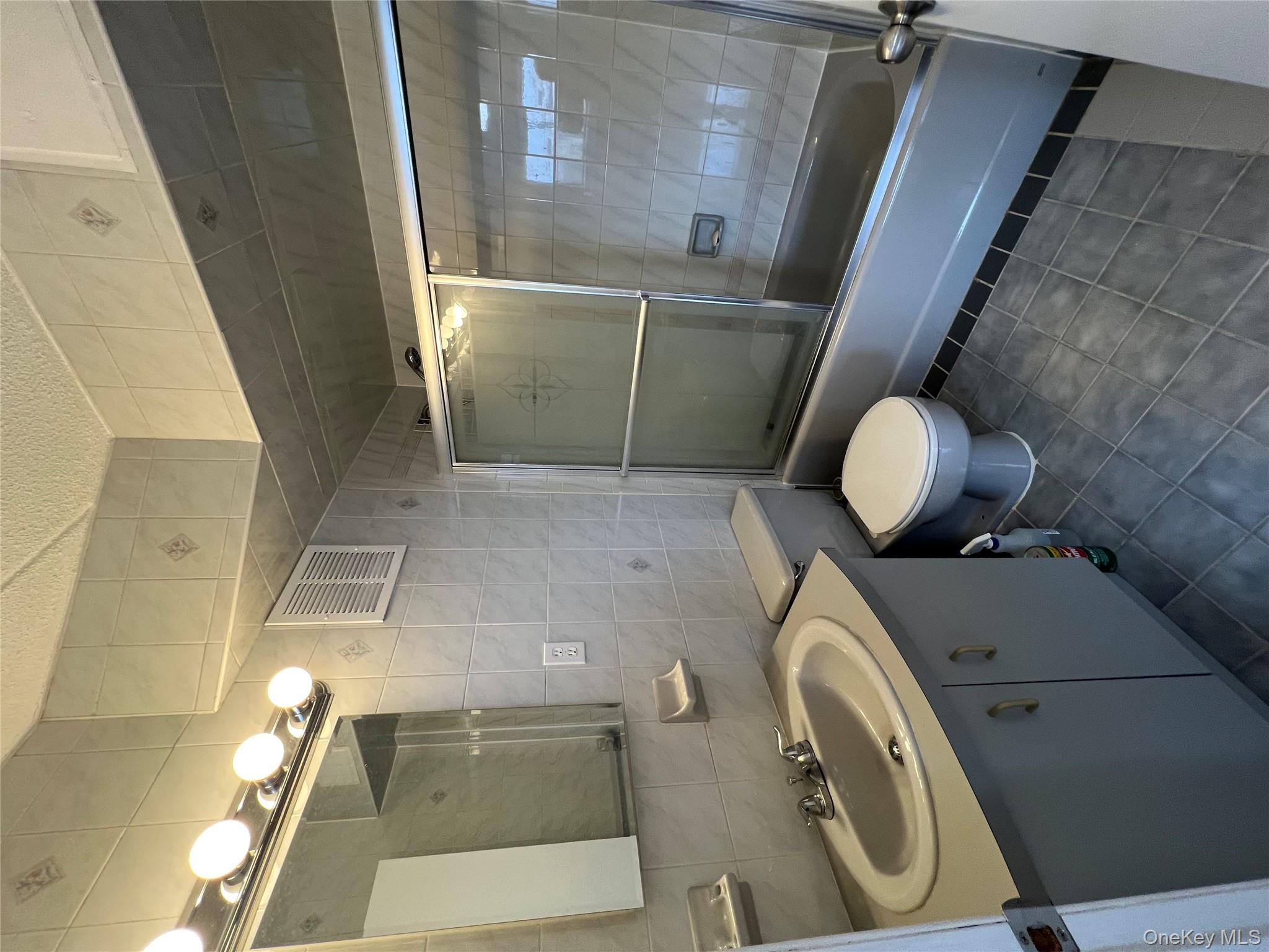 54-09 108th Street, Unit 6A Queens, NY 11368 - Photo 11 of 14 Bathroom featuring tile walls, vanity, dark tile patterned floors, enclosed tub / shower combo, and tasteful backsplash