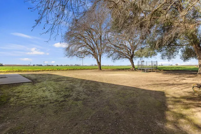 a view of a white house with a big yard plants and large trees