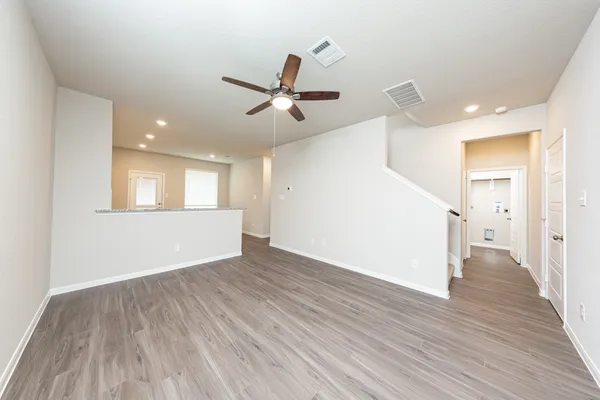 a view of an empty room with wooden floor and a ceiling fan