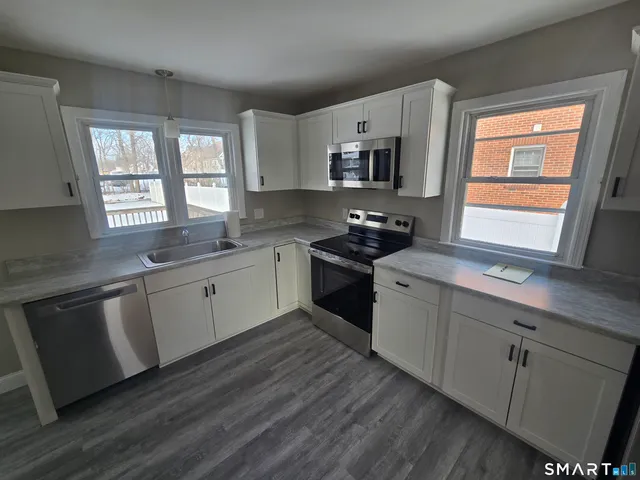 a kitchen with stainless steel appliances granite countertop a sink a stove a refrigerator cabinets and a window