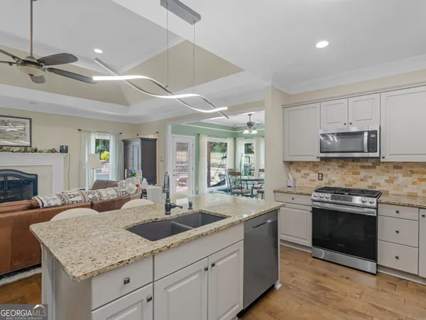 a kitchen with stainless steel appliances granite countertop a refrigerator a sink a stove and white cabinets with wooden floor