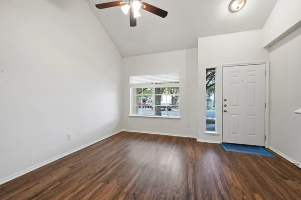 an empty room with wooden floor chandelier fan and windows