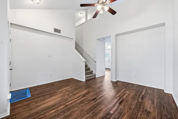 a view of an empty room with wooden floor and a ceiling fan