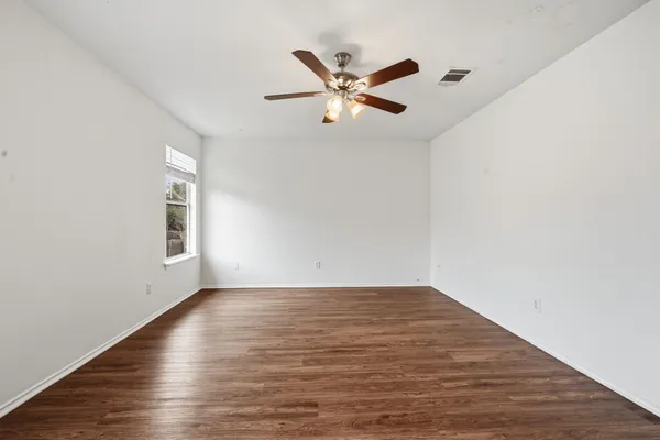 an empty room with wooden floor fan and windows
