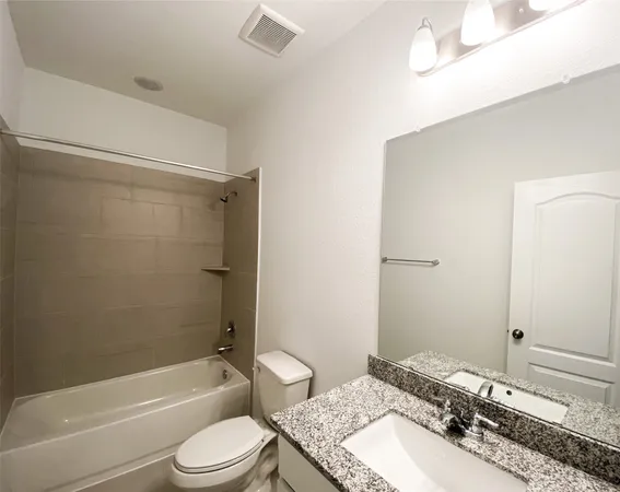 a bathroom with a granite countertop bathtub shower sink vanity mirror and toilet