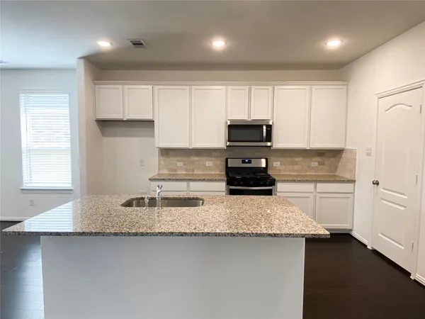a kitchen with kitchen island granite countertop a sink a stove a microwave a counter top and cabinets