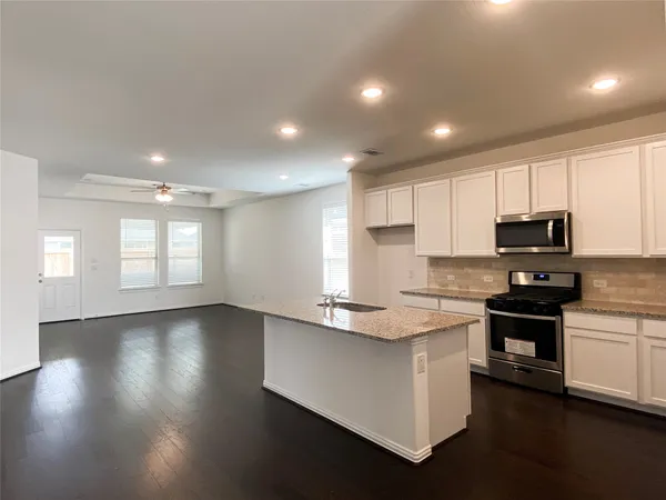 a kitchen with stainless steel appliances granite countertop a stove top oven a sink dishwasher and a refrigerator with wooden floor