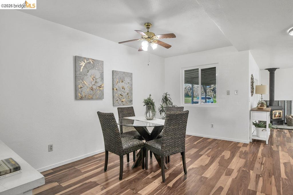 7550 Adams Road Valley Springs, CA 95252 - Photo 15 of 38 Dining room featuring dark wood-style flooring, ceiling fan, and a wood stove